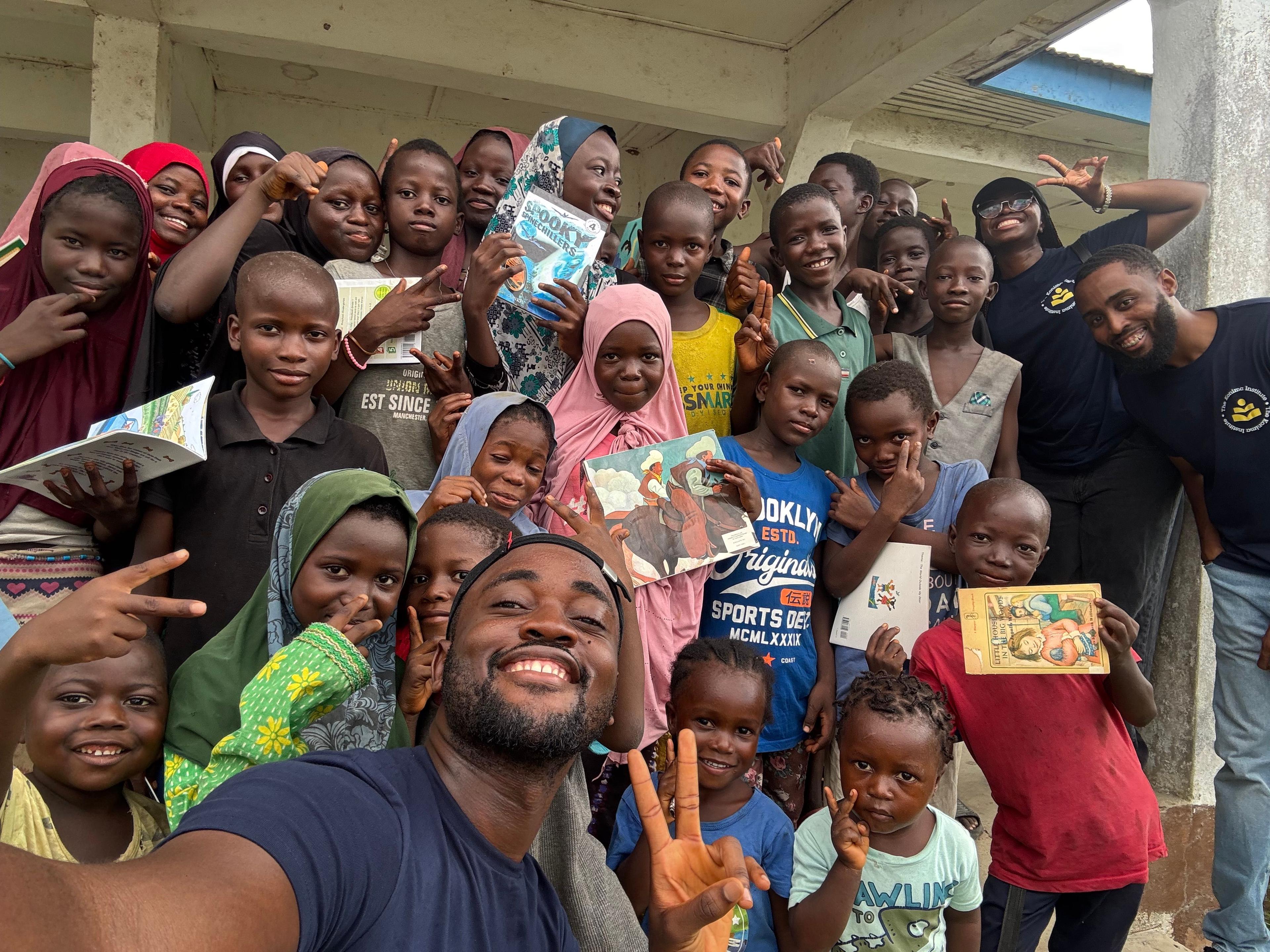 A teacher reads with smiling children gathered in a Sierra Leone courtyard.